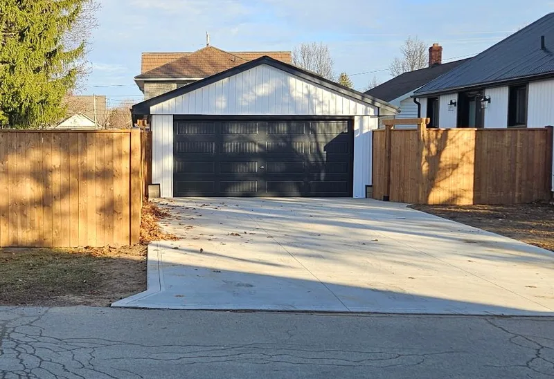 After: the same garage with white siding, a black overhead door and wood fencing