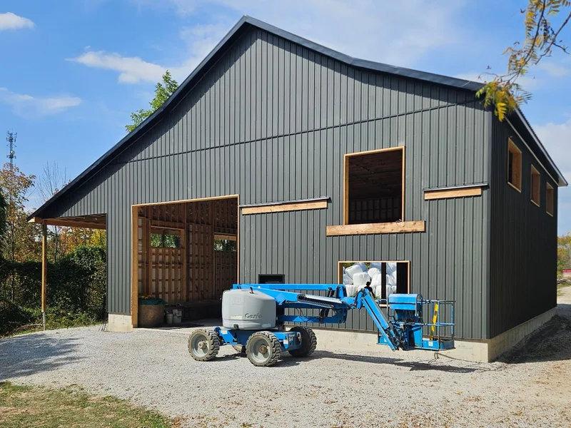 Dark vertical steel siding on a barn, with a lift beside the open door and window openings