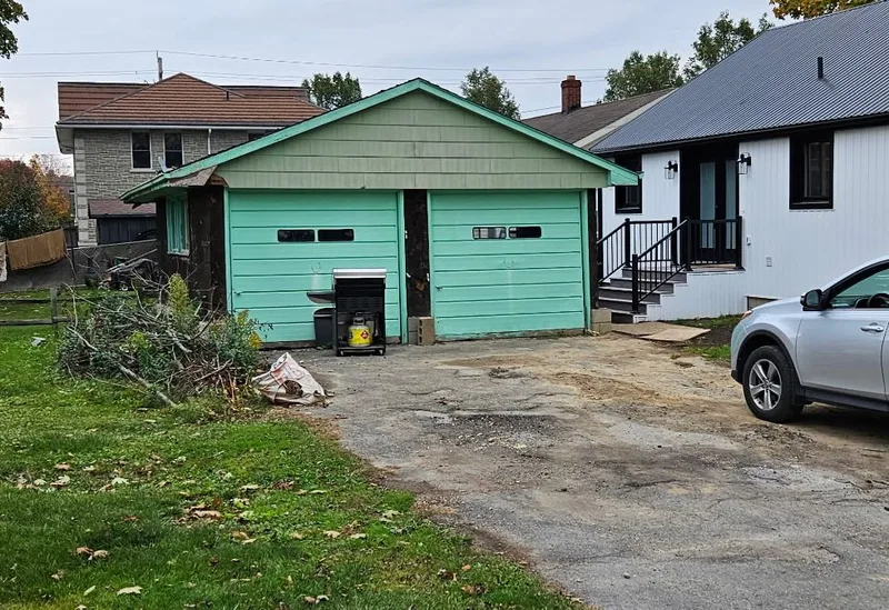 Before: green garage with two overhead doors and an unfenced yard