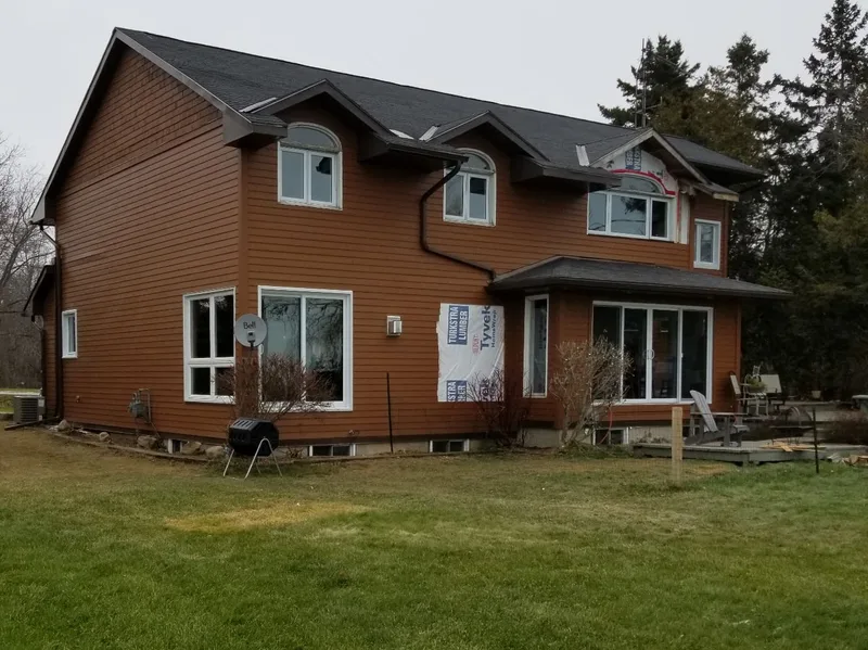 Brown siding installation in progress with exposed house wrap around unfinished areas