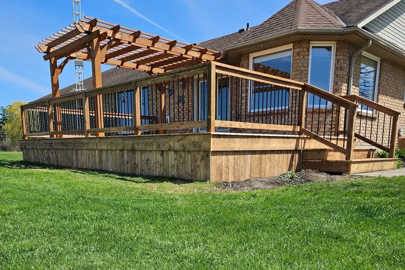 Wood deck with a pergola, railing and stairs beside a house