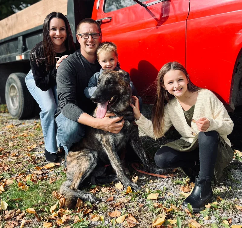 Jeremy and his family with their dog beside a red work truck