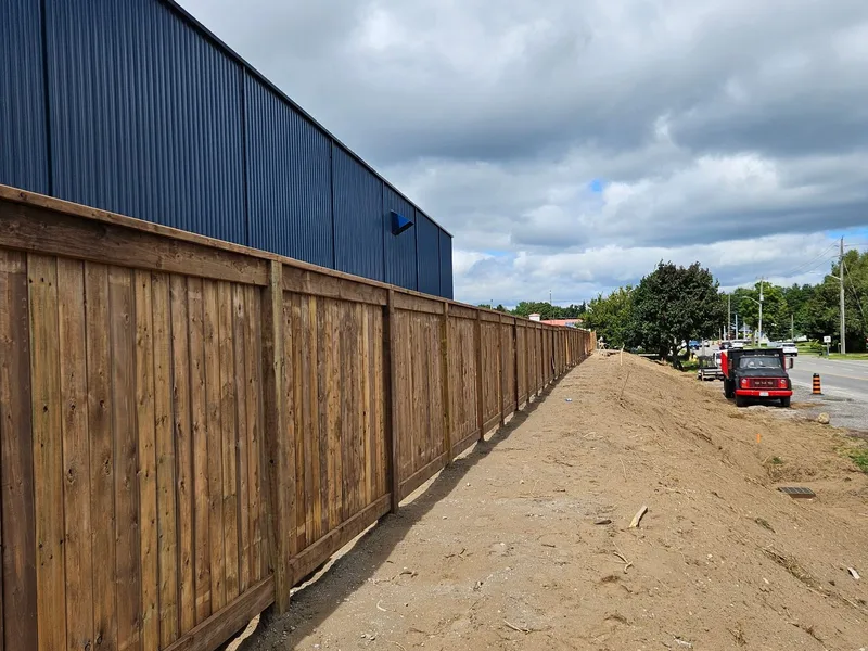 Long wood privacy fence beside a building with blue steel siding