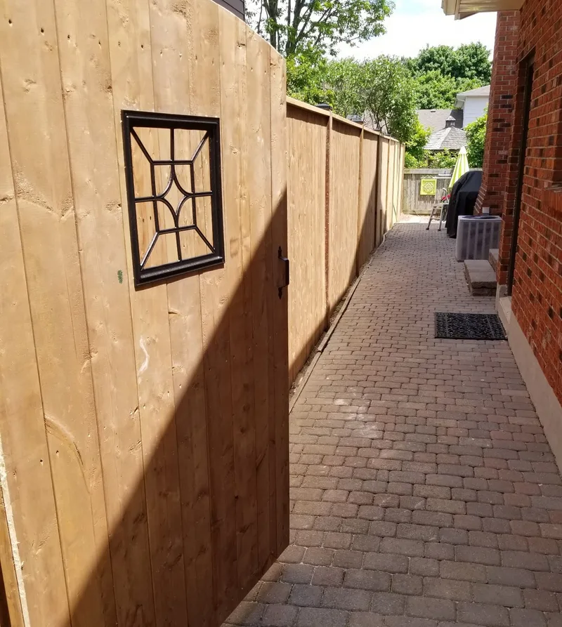 Wood privacy fence and decorative panel beside a brick walkway
