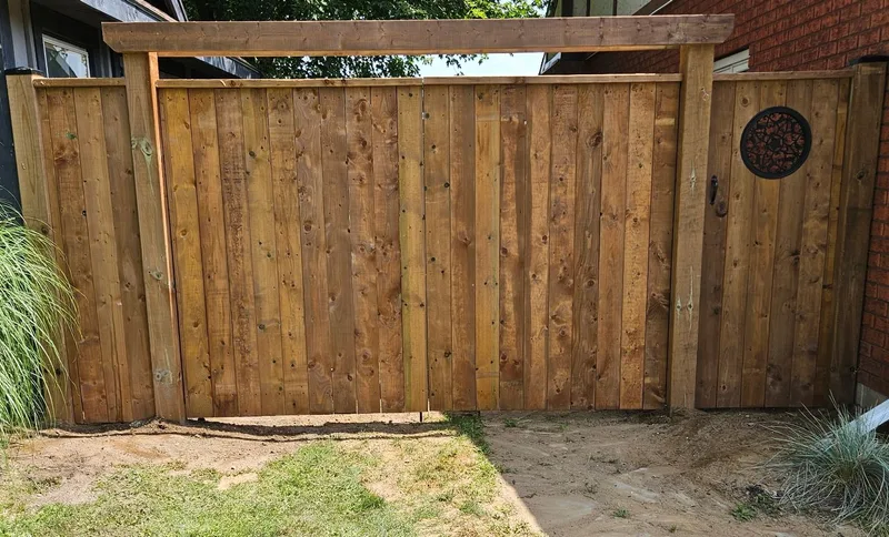 Wood gate with a round decorative opening beside a brick home