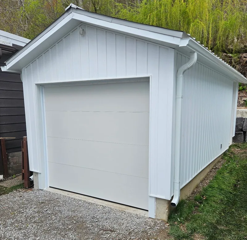 Completed white detached garage with vertical siding and a white overhead door